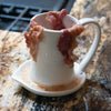Cream-colored ceramic bacon cooker with draped crispy bacon strips resting over the top, designed to catch grease on its base for easy microwave cooking in Kitchen & Food and Kitchen Gadgets collections.