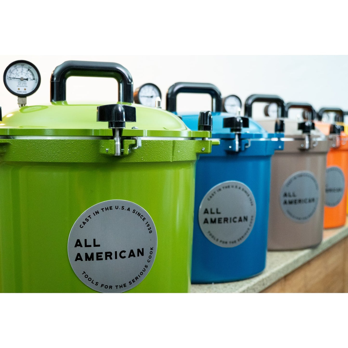 Row of colorful pressure canners in green, blue, taupe, and orange with secure locking lids and pressure gauges, handcrafted for safe food preservation in Kitchen & Food, Canning, Food Preservation, Pressure Canners, USA Made, and Best Sellers collections.