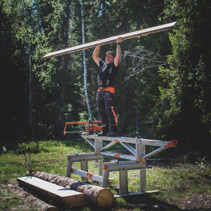 Person standing on a sturdy sawmill frame outdoors in a forest setting, holding a long wooden plank overhead, part of Farm, Garden & Tool, Wood Cutting and Hauling, and Best Sellers collections.
