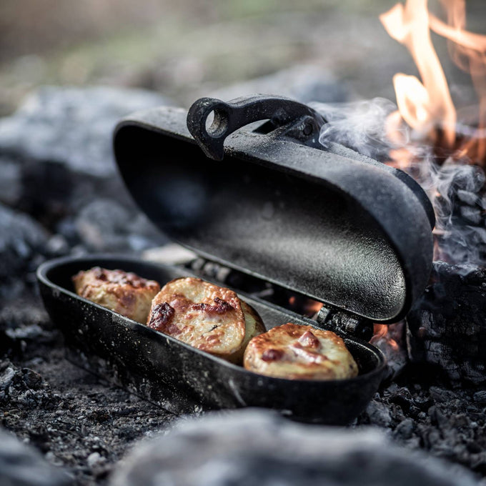 Handcrafted cast iron potato cooker roasting golden potatoes over an open campfire, perfect for outdoor meals, featured in Farm, Garden & Tool, Camping, Best Sellers, and Promo Eligible collections.