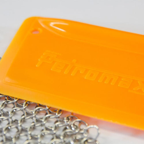 Close-up of bright orange pan scraper with embossed logo and attached metal chain, designed for gentle cleaning of cast iron cookware, featured in Kitchen & Food, Cookware, Cast Iron, Best Sellers, and Promo Eligible collections.