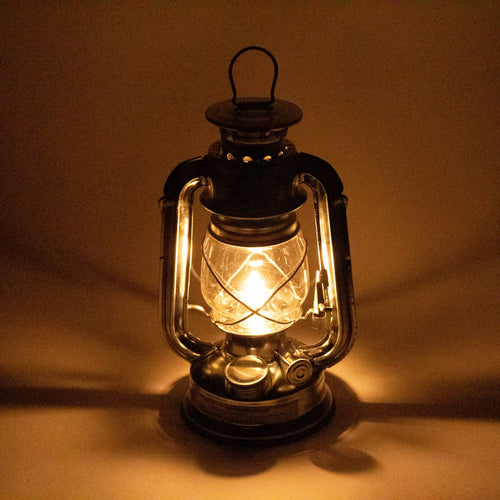 Glowing galvanized race lantern with durable glass and protective wire cage, providing bright, wind-resistant illumination for camping, emergency, and outdoor uses.