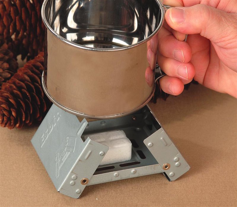 Compact fold-out galvanized steel camping stove burning a solid fuel cube underneath a shiny metal cup held by a hand, ideal for Farm, Garden & Tool, Camping, and Emergency Supplies collections.
