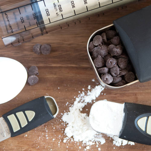Adjustable measuring cups and spoons with black handles, shown with spilled flour and chocolate chips, ideal for Kitchen & Food, Food Prep, Measuring, and Kitchen Gadgets collections.