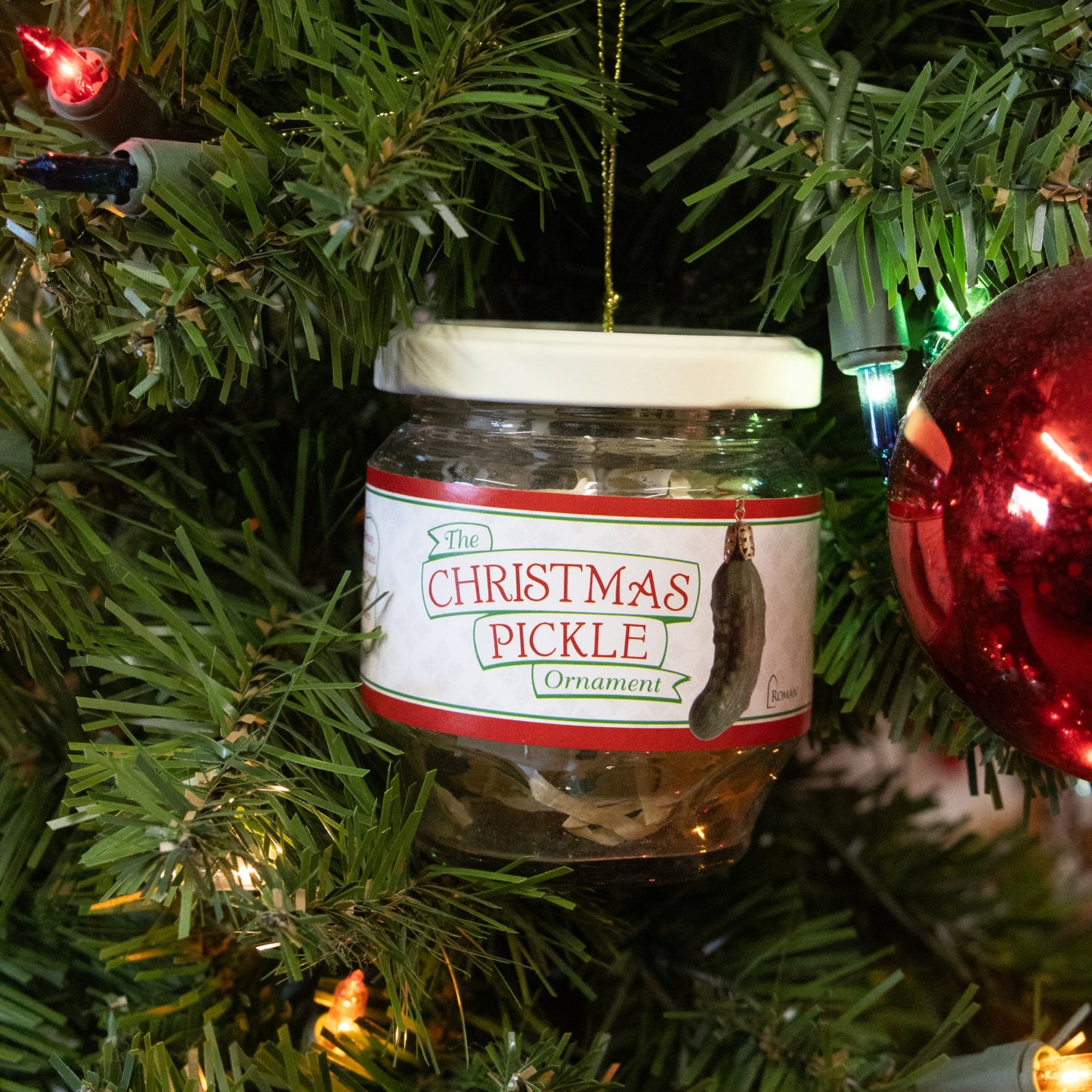 Glass jar ornament featuring a Christmas pickle replica hanging on a tree with gold string, embraced by holiday lights and traditional Christmas decor in Home & Decor.