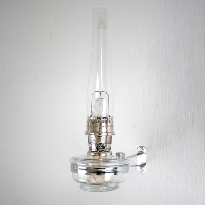 Clear glass oil lamp with tall chimney mounted on a shiny metal wall bracket, designed for use with classic Aladdin lamps in Lamps & Lighting, Oil Lamps, Wall Lamps, Best Sellers, and Promo Eligible collections.