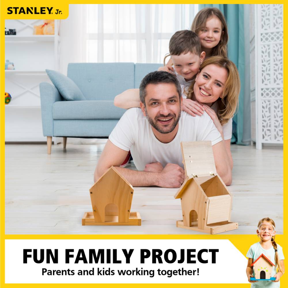 Family of four smiling and lying on the floor indoors with two wooden bird feeders in front of them, highlighting a hands-on DIY project from the Toys, Books & Games and Arts and Crafts collections.