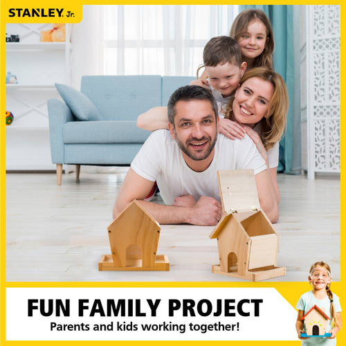Family of four smiling and lying on the floor indoors with two wooden bird feeders in front of them, highlighting a hands-on DIY project from the Toys, Books & Games and Arts and Crafts collections.
