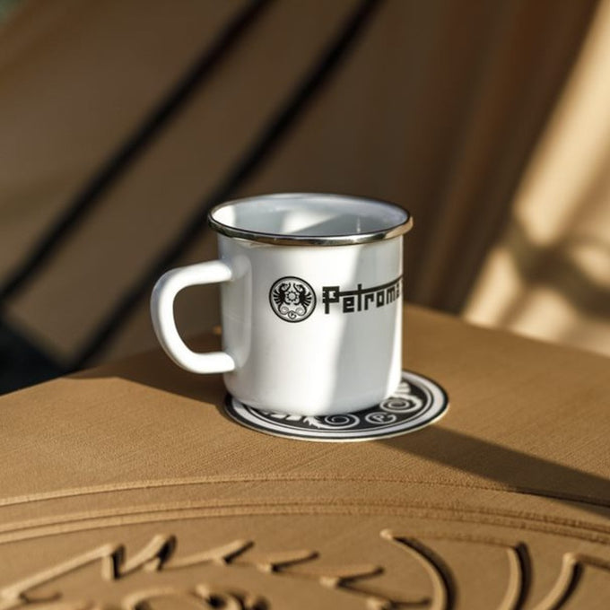 White enameled steel mug with metal rim and black logo, sitting on embossed surface, perfect for Farm, Garden & Tool, Camping, Brewing Coffee and Tea, Kitchen & Food, Dinnerware, and Best Sellers collections.