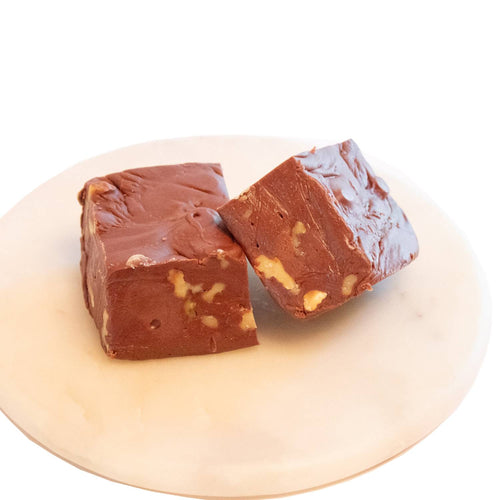 Two handcrafted rich chocolate fudge pieces with visible walnut chunks, presented on a smooth white plate, featured in Kitchen & Food, Snacks and Sweets, USA Made, Best Sellers, and Promo Eligible collections.