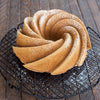 Golden-brown swirl cake with powdered sugar dusting, cooled on a black wire rack on a rustic wooden surface, highlighting elegant baking for Kitchen & Food and Baking Supplies.