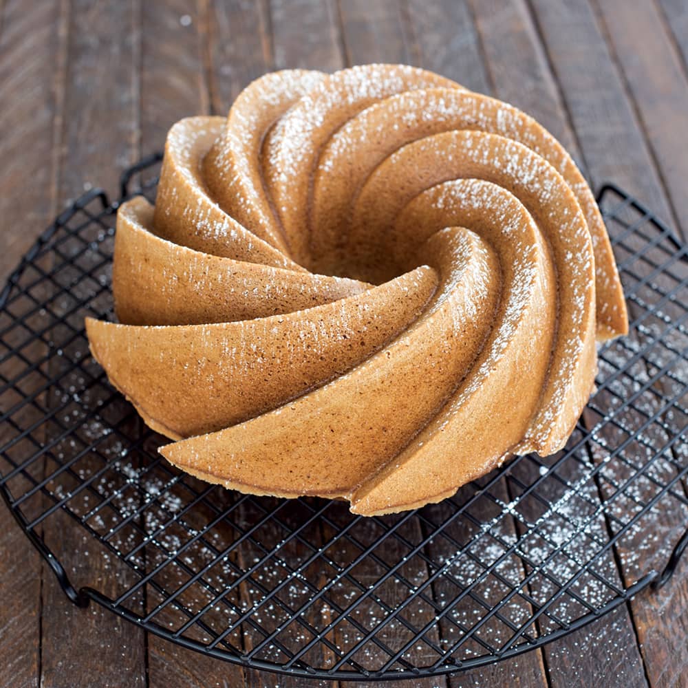 Golden-brown swirl cake with powdered sugar dusting, cooled on a black wire rack on a rustic wooden surface, highlighting elegant baking for Kitchen & Food and Baking Supplies.