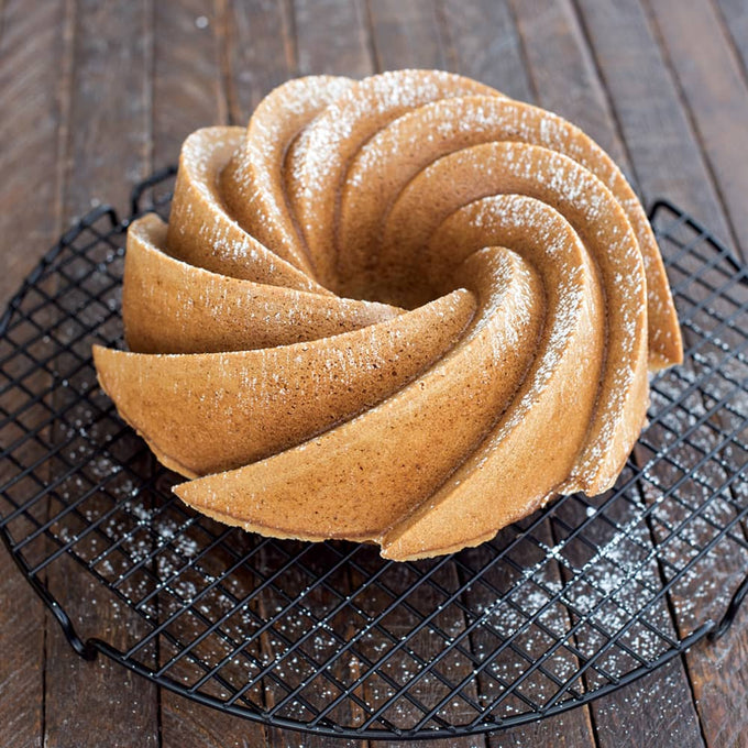 Golden-brown swirl cake with powdered sugar dusting, cooled on a black wire rack on a rustic wooden surface, highlighting elegant baking for Kitchen & Food and Baking Supplies.