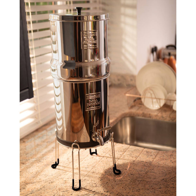 Stainless steel gravity water filter system elevated on a sleek stand with rubber-tipped legs, designed for easy dispensing and kitchen counter convenience, featured in Appliances and Emergency Supplies collections.