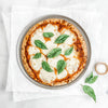 12-inch aluminized steel pizza pan with a crispy crust and melted cheese topped with fresh basil leaves, styled for Kitchen & Food, Cookware, and USA Made collections.