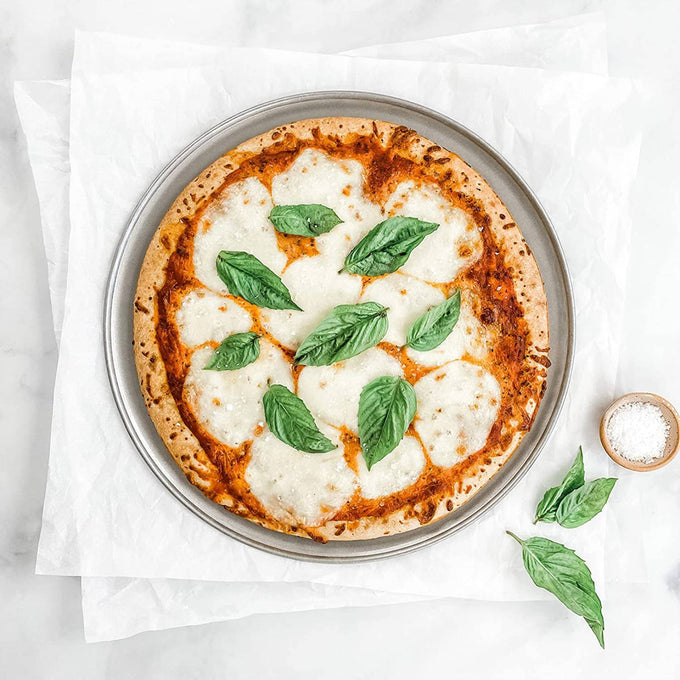 12-inch aluminized steel pizza pan with a crispy crust and melted cheese topped with fresh basil leaves, styled for Kitchen & Food, Cookware, and USA Made collections.