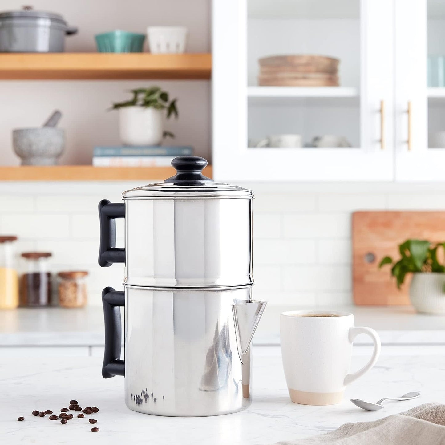 Stainless steel non-electric drip coffee maker with black handles on a white kitchen countertop, surrounded by coffee beans, a white mug, and a spoon, featured in Farm, Garden & Tool and Kitchen & Food collections.