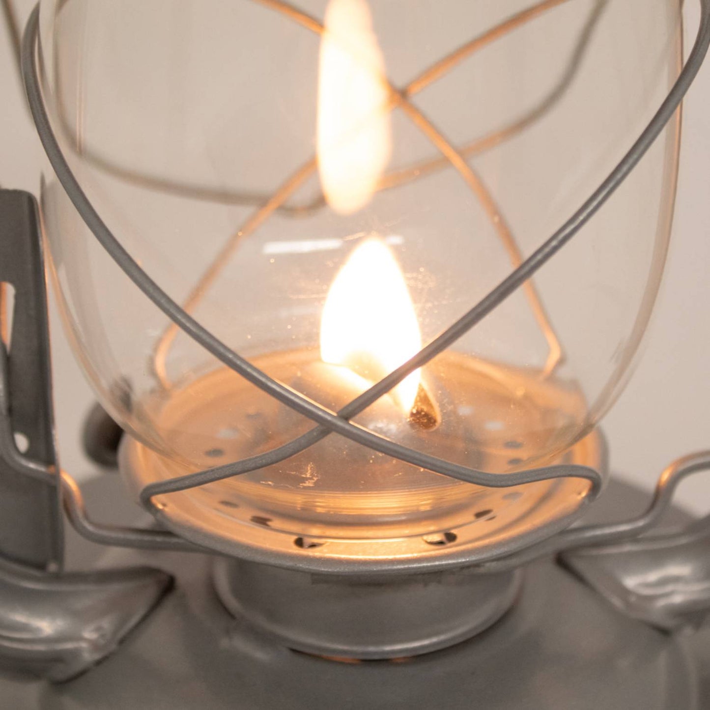 Close-up of a handcrafted metal lantern’s glass globe and flame protected by a sturdy wire frame, ideal for reliable lighting in farm, garden, camping, and emergency use.