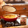 Person lifting lid of red pot with soup or stew made from broth with noodles, next to can of Lehman’s handcrafted beef broth on stovetop in rustic kitchen, featured for Farm, Garden & Tool, Kitchen & Food, Emergency Supplies, Food, Meats, Best Sellers, and Promo Eligible collections.