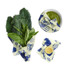 Set of three reusable beeswax food wraps in cream with blue bee and honeycomb designs, covering fresh greens, a bowl of green sauce, and a halved lemon, eco-friendly and handmade in USA collections.