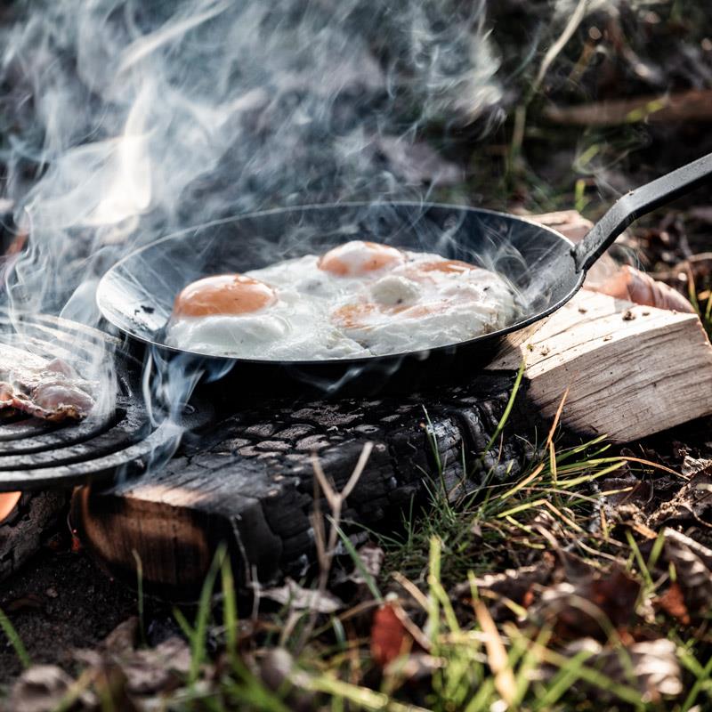 Petromax wrought iron pan with long handle cooking eggs over an open fire outdoors, showcasing durable cookware ideal for Farm, Garden & Tool, Kitchen & Food, Camping, and Best Sellers collections.