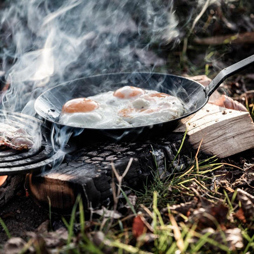 Petromax wrought iron pan with long handle cooking eggs over an open fire outdoors, showcasing durable cookware ideal for Farm, Garden & Tool, Kitchen & Food, Camping, and Best Sellers collections.