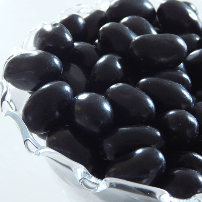 Close-up of large smooth black licorice jelly beans piled in a clear glass bowl, featured in Kitchen & Food, Snacks and Sweets, and Best Sellers collections.