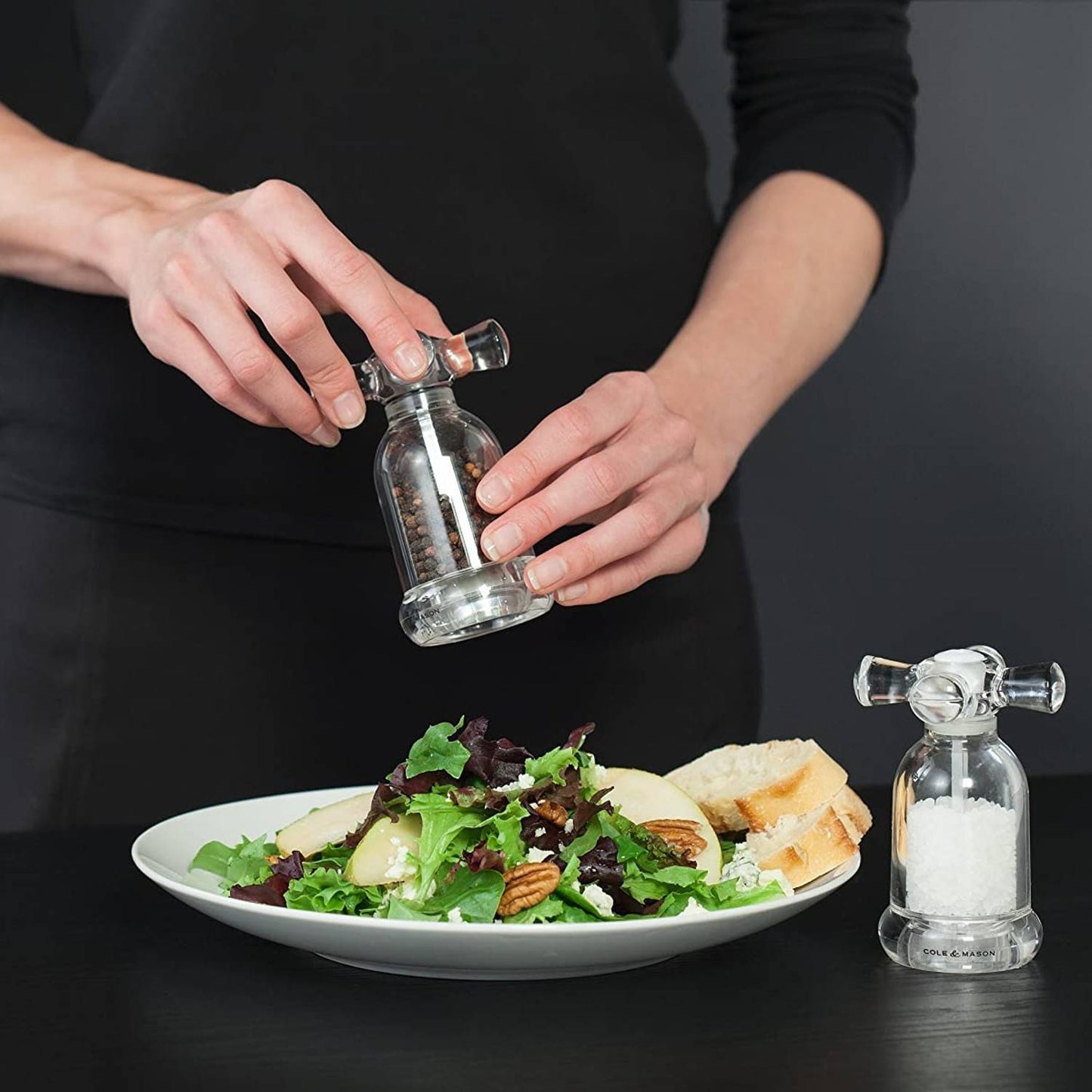 Clear acrylic mills styled like vintage faucet handles, one grinding fine peppercorns over a fresh salad with bread, the other filled with coarse sea salt, ideal for Kitchen & Food, Dinnerware, Storage and Serving, Best Sellers, and Promo Eligible collections.