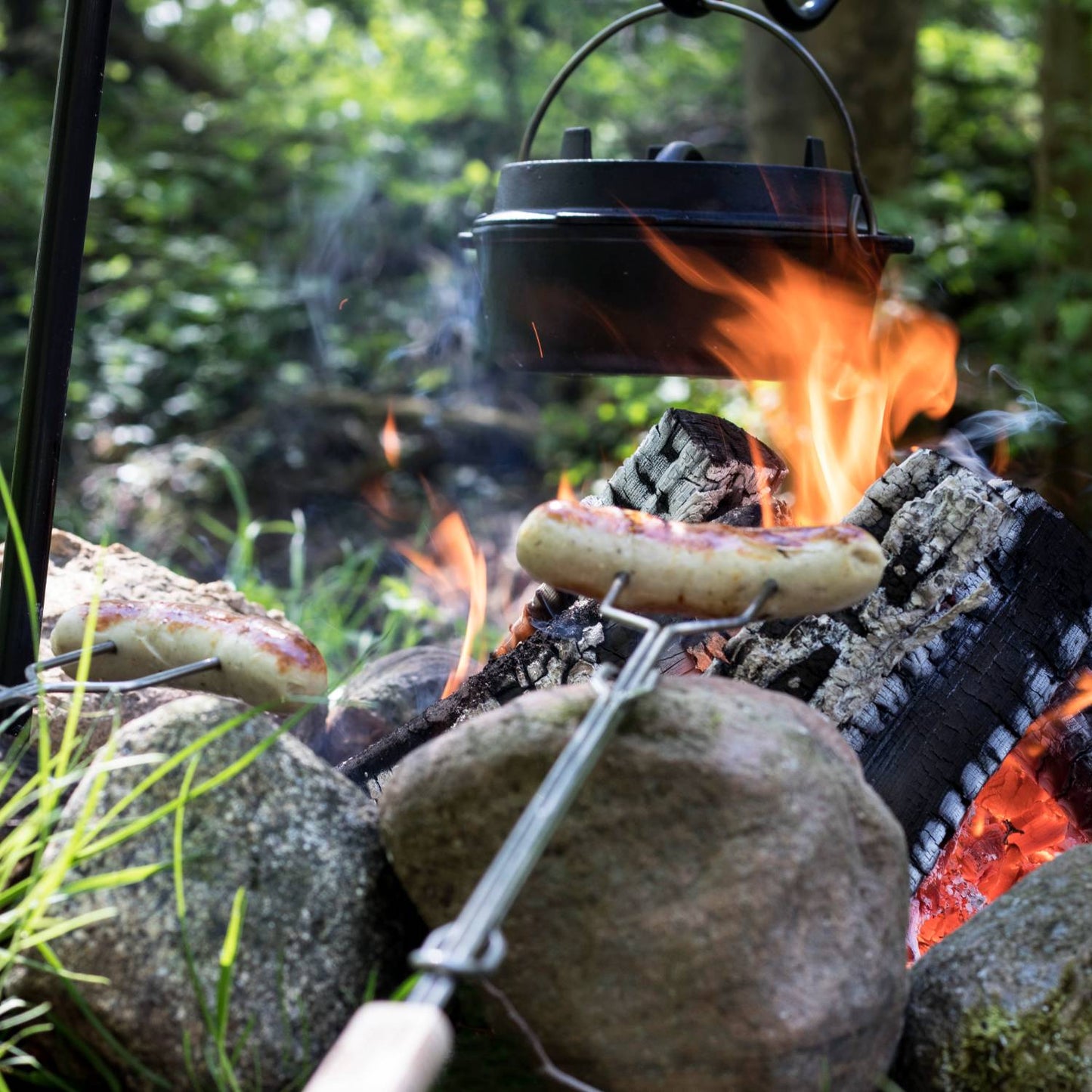 Handcrafted campfire skewer with adjustable metal shaft and wooden handle roasting sausages over a natural stone fire pit, perfect for Farm, Garden & Tool, Camping, Best Sellers, Promo Eligible collections.
