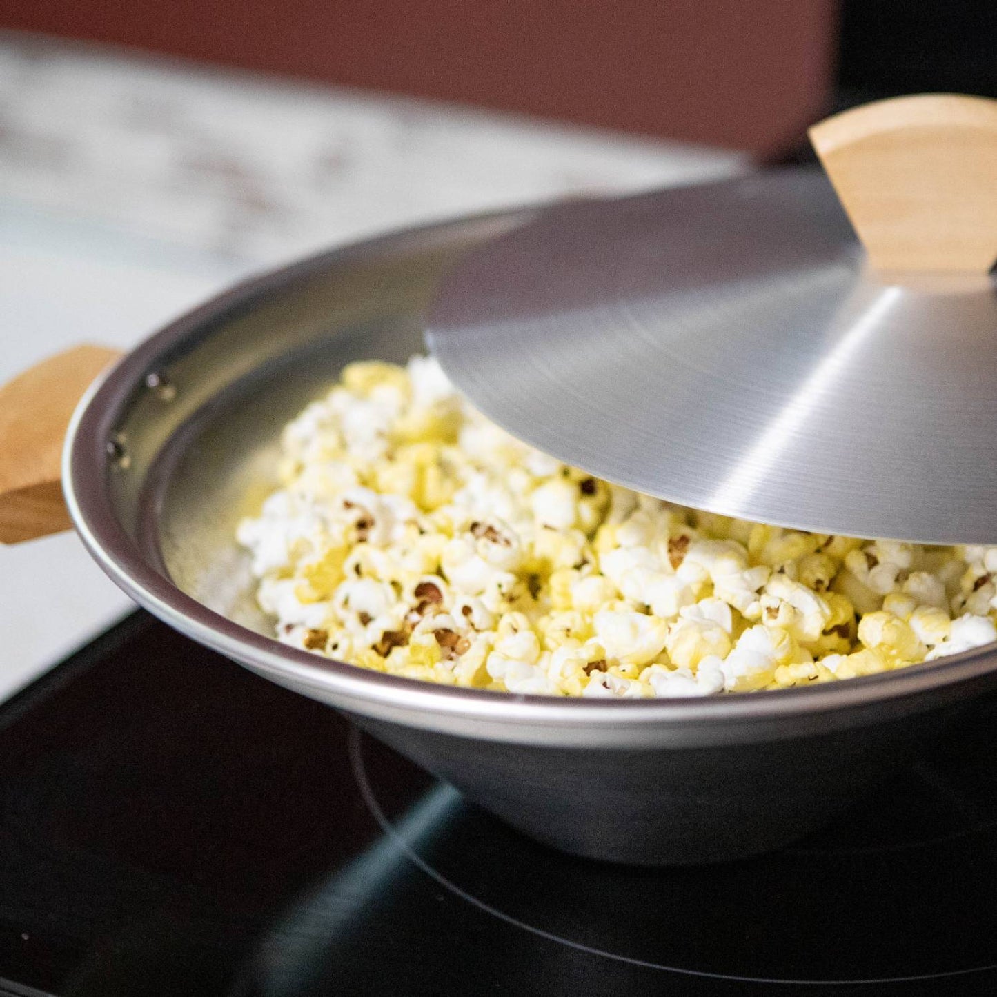 Close-up of a lightweight aluminum stovetop popcorn popper with partially open lid and wooden handles, filled with freshly popped popcorn, featured in Kitchen & Food, Cookware, and Popcorn collections.