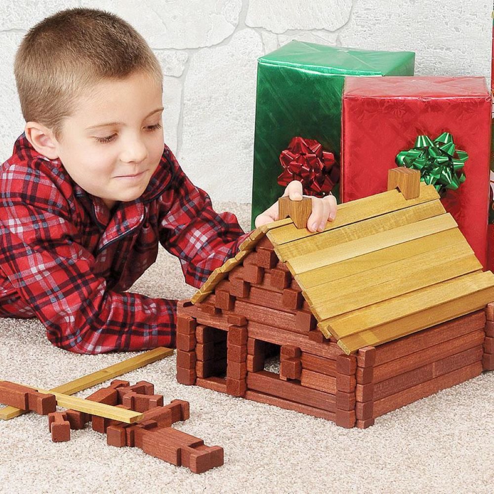 Young boy building a handcrafted wooden log cabin toy indoors, featuring durable hardwood construction with non-toxic stain, part of USA Made, Amish Made, and Toys, Books & Games collections.