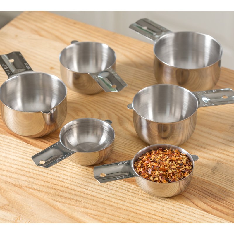 Set of six durable 18/8 stainless steel nesting measuring cups arranged on a wooden surface with one cup filled with crushed red pepper flakes, perfect for Kitchen & Food, Baking Supplies, and Food Prep collections.
