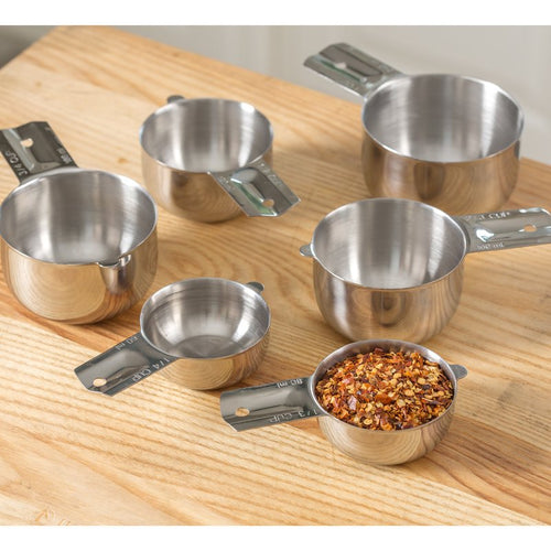 Set of six durable 18/8 stainless steel nesting measuring cups arranged on a wooden surface with one cup filled with crushed red pepper flakes, perfect for Kitchen & Food, Baking Supplies, and Food Prep collections.