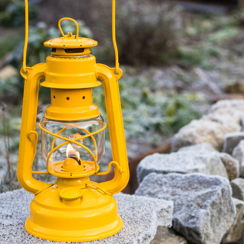 Handcrafted yellow galvanized oil lantern with robust metal design and thermal heat-resistant globe, glowing softly outdoors on a stone surface in Camping, Lamps & Lighting, Emergency Supplies collections.