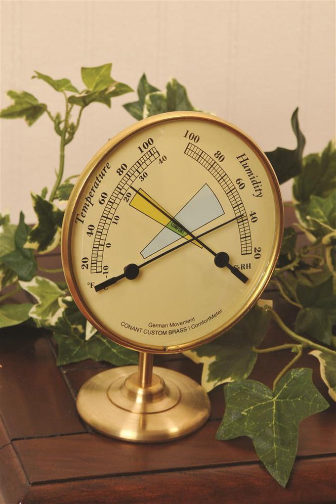 Brass hygrometer and thermometer with dual dials measuring temperature in Fahrenheit and Celsius and relative humidity, displayed on a round stand amid green ivy, ideal for Home & Decor and Household Helpers collections.