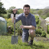 Man kneeling in garden holding a heavy-duty treaded digging spade with a solid forged carbon steel head and ergonomic handle, ideal for Farm, Garden & Tool, Digging and Cultivating, Lawncare, Best Sellers, and Promo Eligible collections.