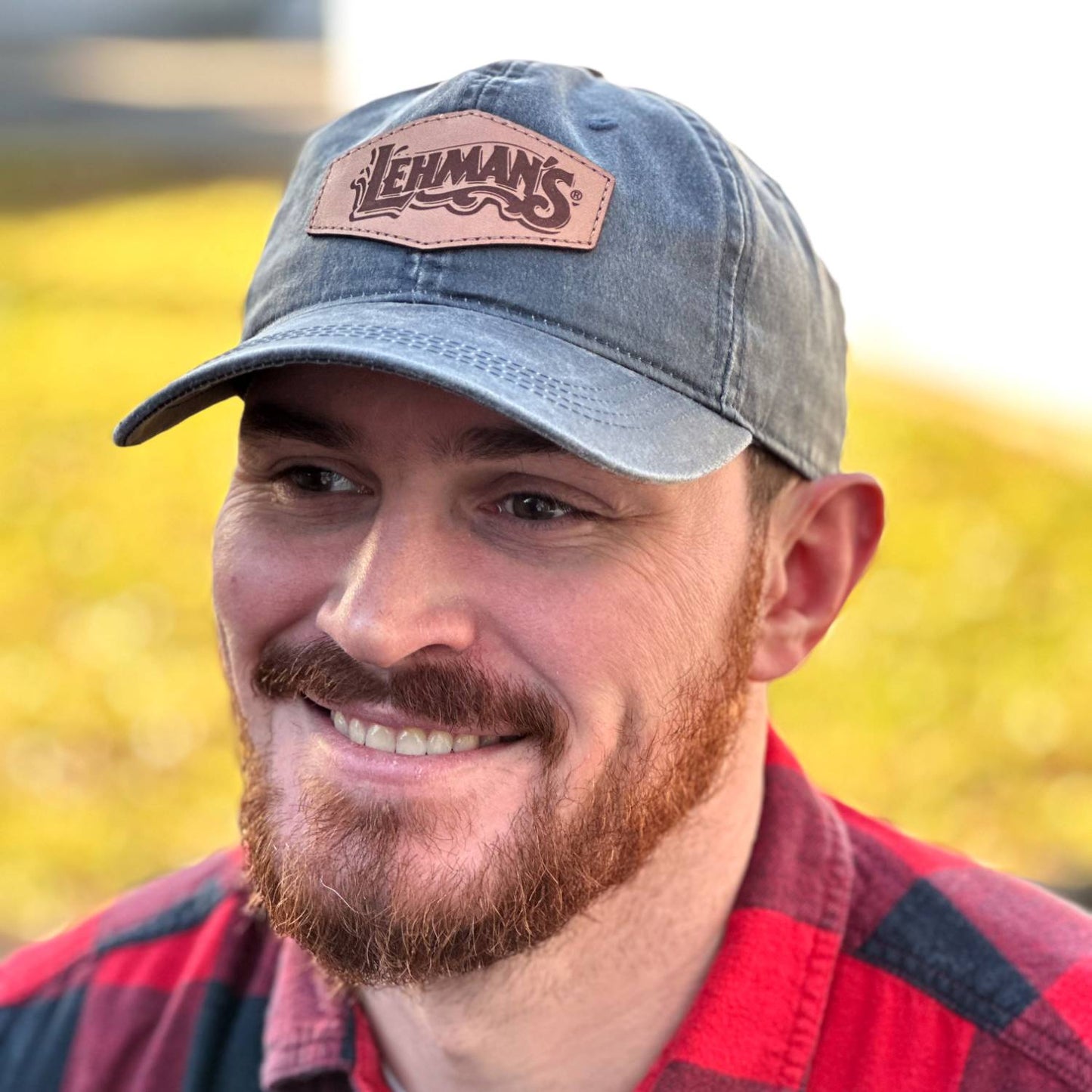 Man outdoors smiling wearing an adjustable vintage-style washed cotton cap with a pre-curved visor and light brown leather patch, handcrafted and ideal for Health & Wellness and Best Sellers collections.
