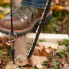 Close-up of a compact pocket chain saw cutting through a small limb on the ground, with a work boot in the background, perfect for Farm, Garden & Tool and Camping gear collections.