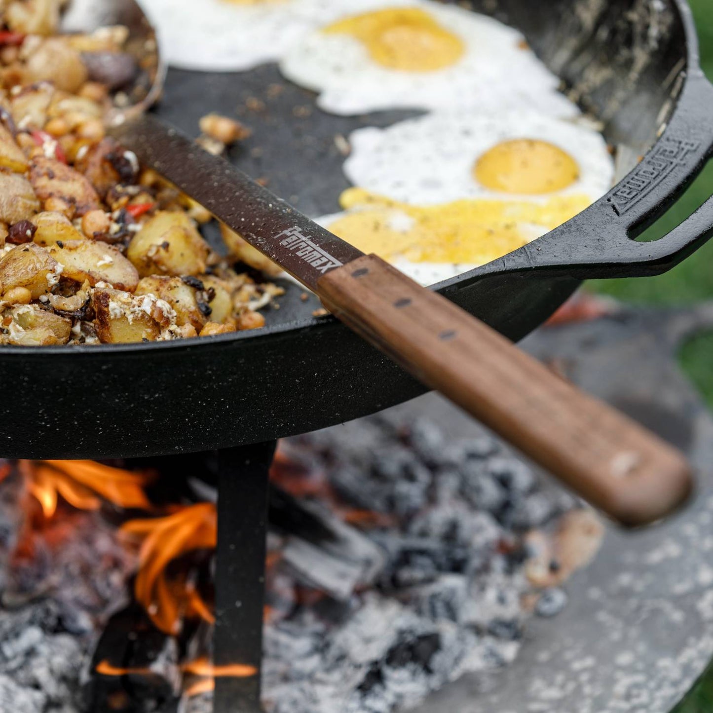 Long stainless steel serving spoon with a smooth walnut handle resting in a cast iron skillet with cooked potatoes and eggs over an open campfire, ideal for Farm, Garden & Tool, Kitchen & Food, Camping, Storage and Serving, Best Sellers, Promo Eligible collections.