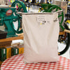 Large 25-pound white paper bag of organic hulled barley groats placed on a red and white checkered tablecloth, surrounded by grain mills, in Farm, Garden & Tool and Pantry collections.