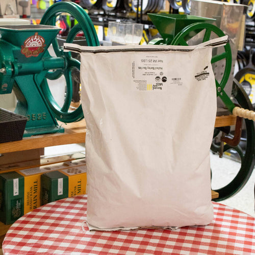Large 25-pound white paper bag of organic hulled barley groats placed on a red and white checkered tablecloth, surrounded by grain mills, in Farm, Garden & Tool and Pantry collections.