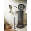 Wall-mounted kindling splitter holding wood next to a lit vintage cast iron stove with a basket of firewood on a wooden floor, ideal for Farm, Garden & Tool and Wood Cutting collections.