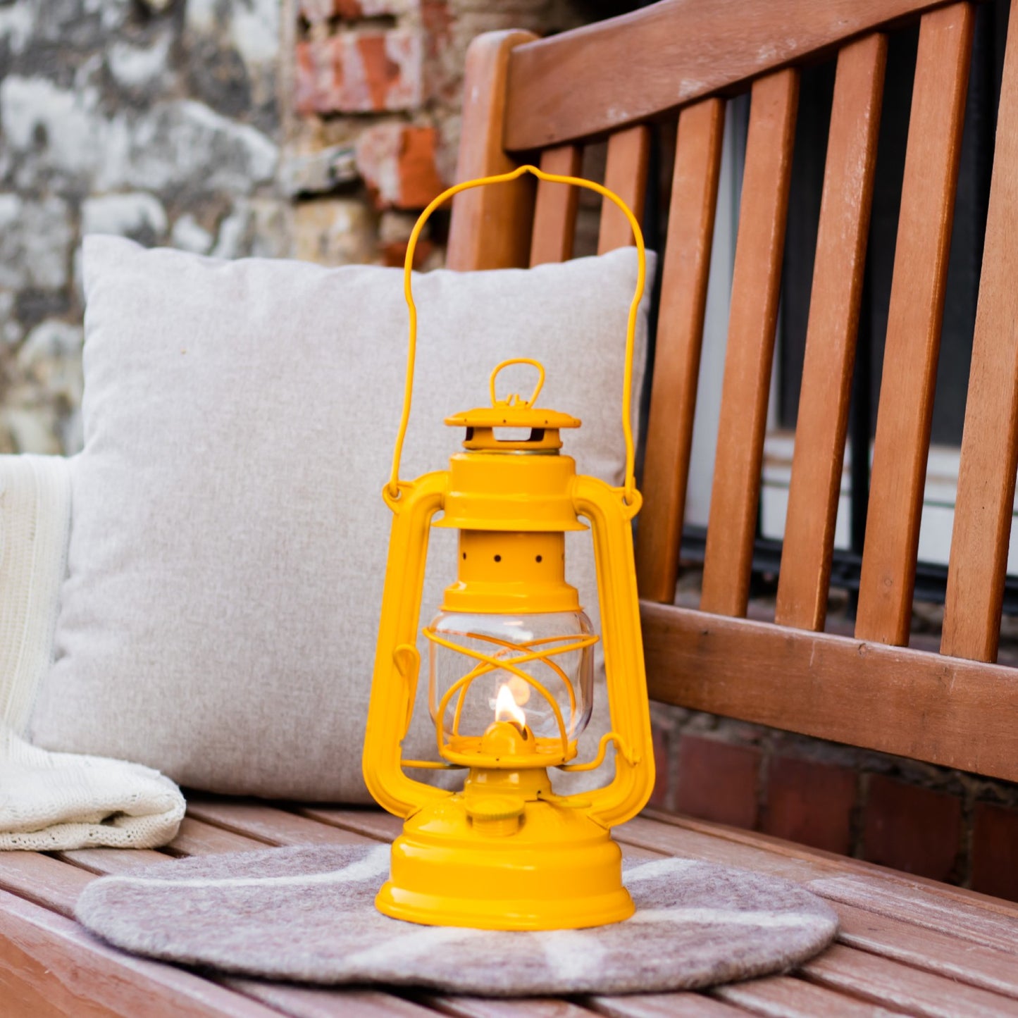 Handcrafted bright yellow galvanized oil lantern emitting warm light, placed on a cozy cushion atop a wooden bench, perfect for Lamps & Lighting, Camping, and Emergency Supplies collections.