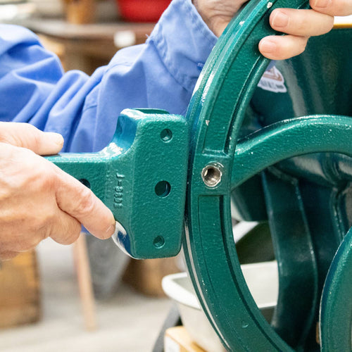 Close-up of a person attaching a sturdy green metal handle extension to a grain mill wheel, enhancing leverage for easier grinding, ideal for Kitchen & Food and Bread Making Supplies collections.