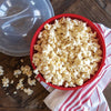 Red BPA-free microwavable bowl filled with freshly popped popcorn, accompanied by a clear vented lid and striped kitchen towel, ideal for Kitchen & Food, Popcorn, and Cooking and Baking Helpers collections.