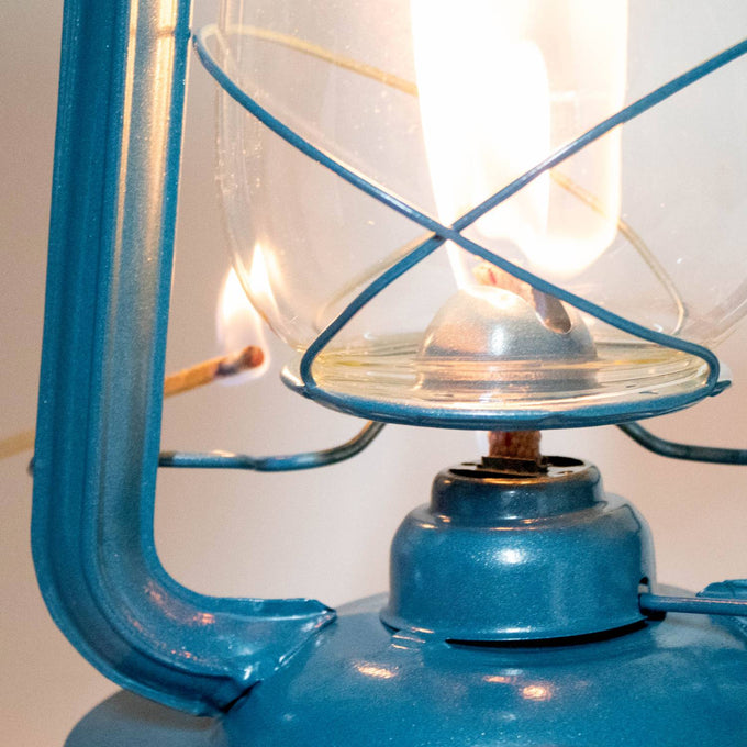Close-up of a handcrafted blue lantern being lit with a match, showcasing its sturdy metal frame and glass globe, perfect for Farm, Garden & Tool, Camping, and Emergency Supplies collections