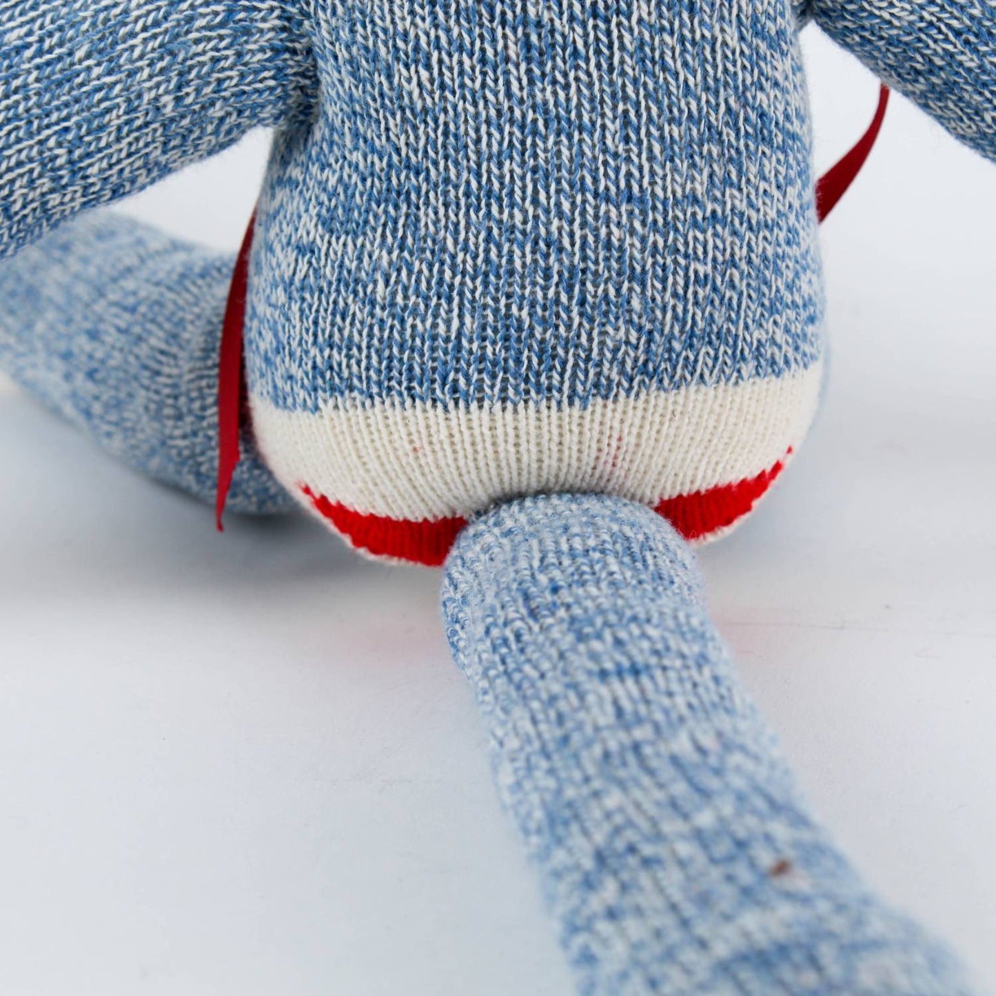 Close-up of a handcrafted sock monkey’s lower body in blue knit with red and white heel sock detail and a flexible tail, featured in Toys, Books & Games and USA Made collections.