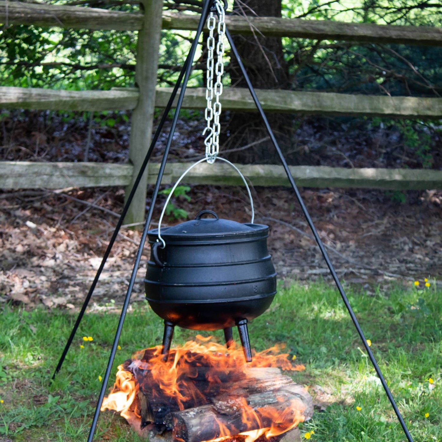 Unique handcrafted cast iron campfire kettle with a round body and three legs, hanging from a tripod chain over an open fire, ideal for Farm, Garden & Tool, Camping, Best Sellers, and Promo Eligible collections.