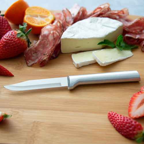 Sharp carbon stainless steel paring knife with a satin-finished cast aluminum handle resting on a wooden board surrounded by sliced strawberries, orange, salami, and creamy cheese, ideal for food prep in USA made and best sellers collections.