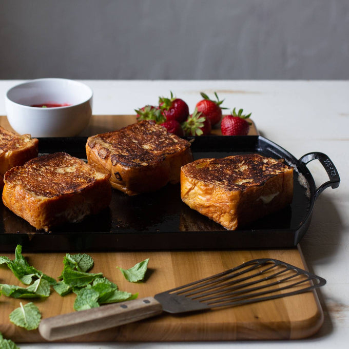 Close-up of three golden-brown toasted sandwiches cooking on a lightweight cast iron double burner griddle with side handles, accompanied by fresh strawberries, mint leaves, and a metal spatula on a wooden board, featured in Kitchen & Food, Cookware, Cast Iron, USA Made, and Best Sellers collections.